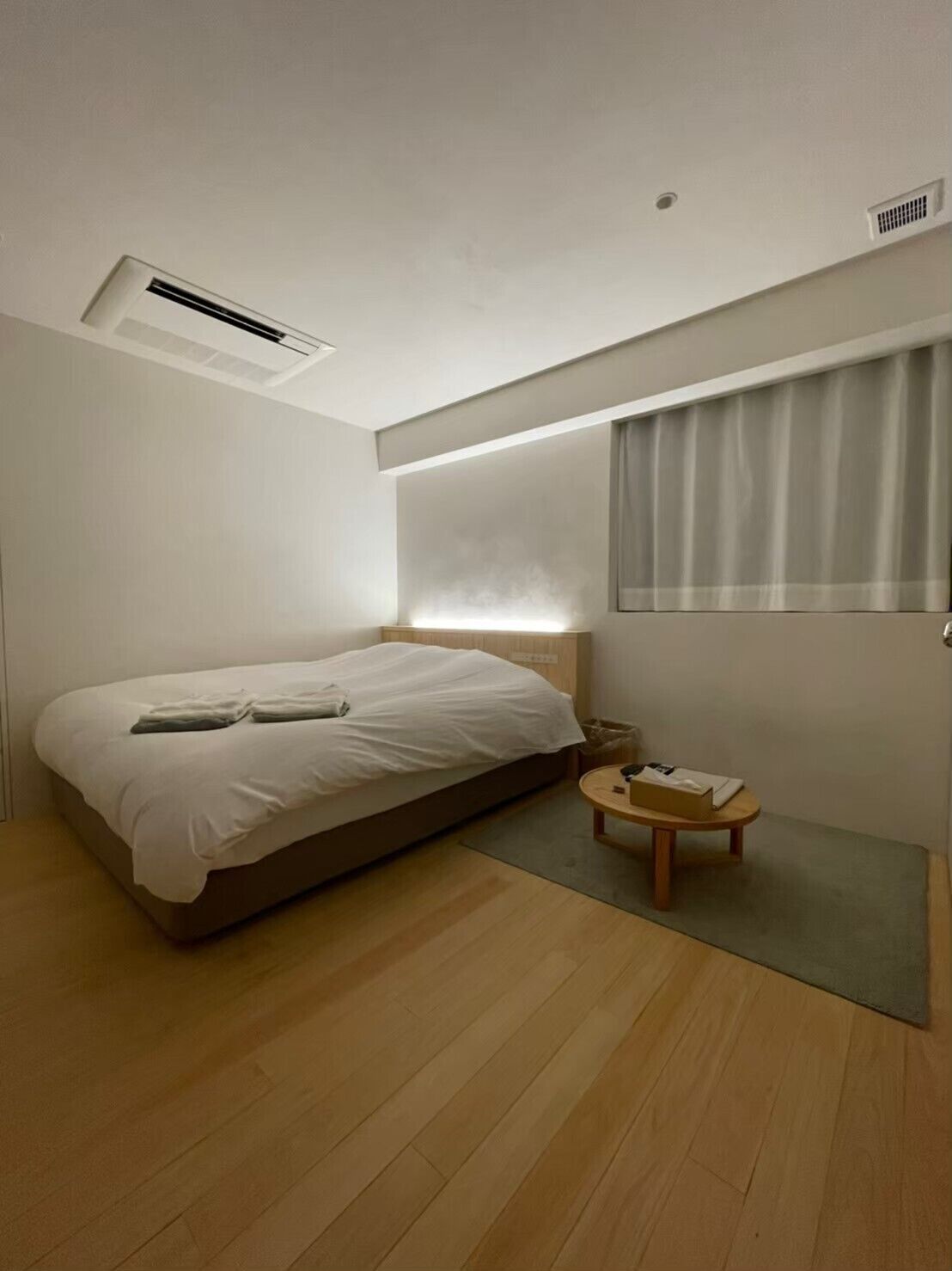 A modern hotel room with a single bed, a small round table, and a window with curtains.