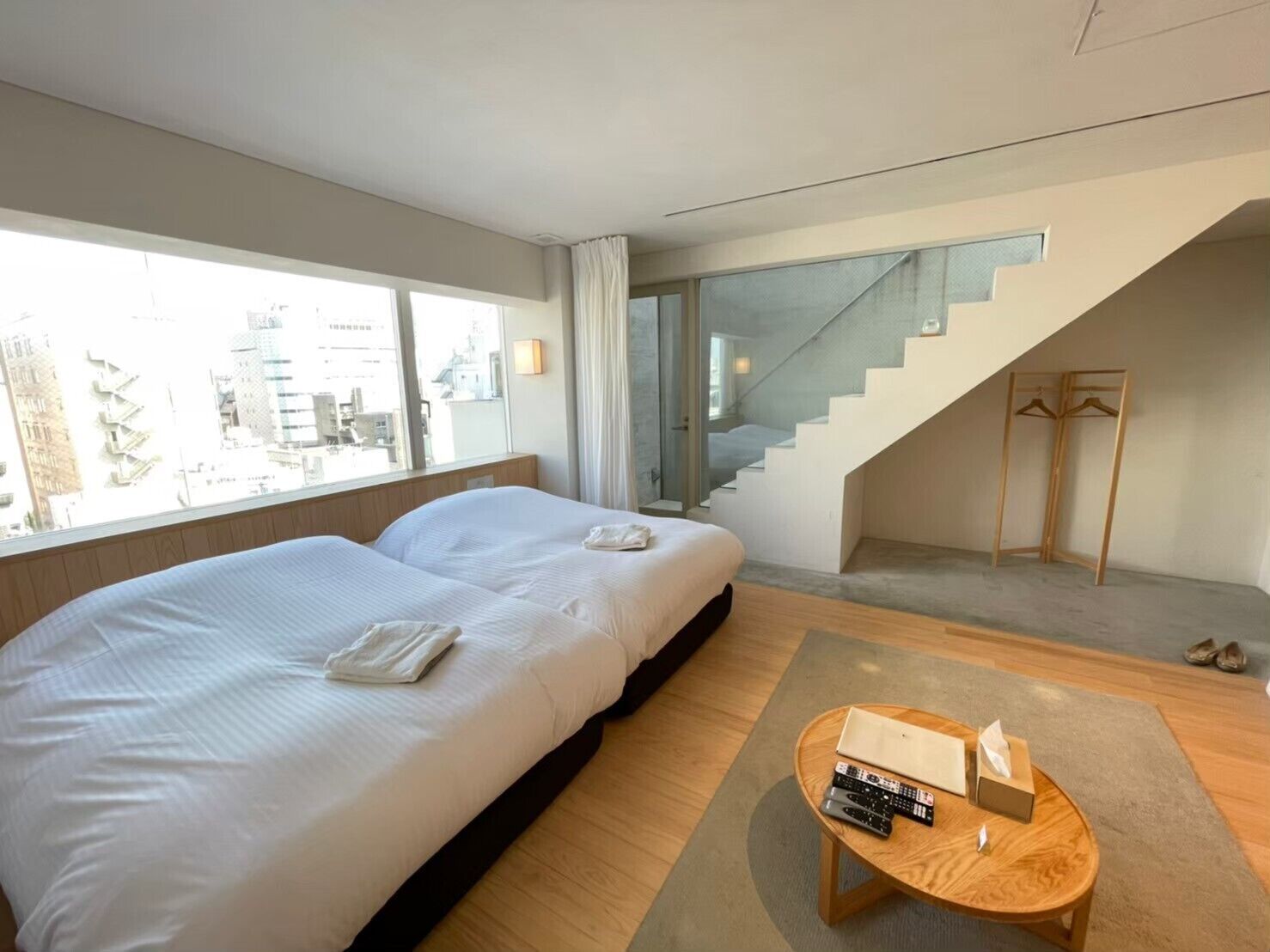 A modern hotel room with two beds, a staircase, and a view of the city.