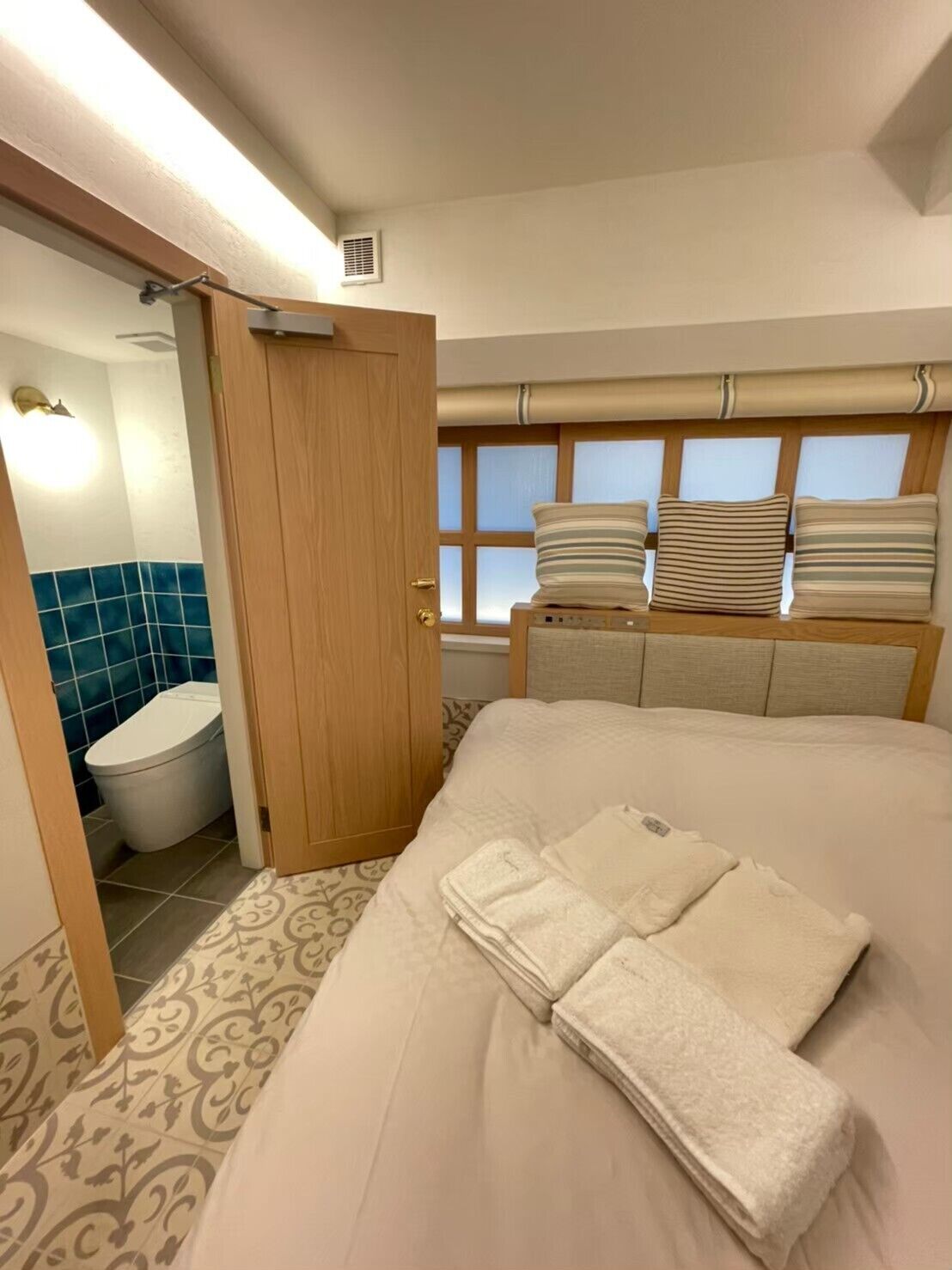 A hotel room with a bed, a bathroom, and a window with blinds.