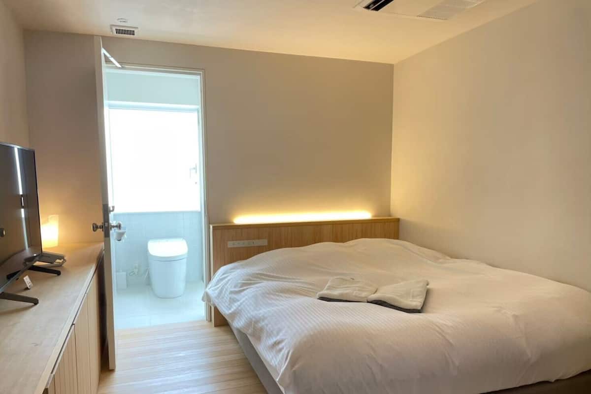 Une chambre à coucher comprenant un lit, une table de chevet et une porte donnant sur une salle de bain.