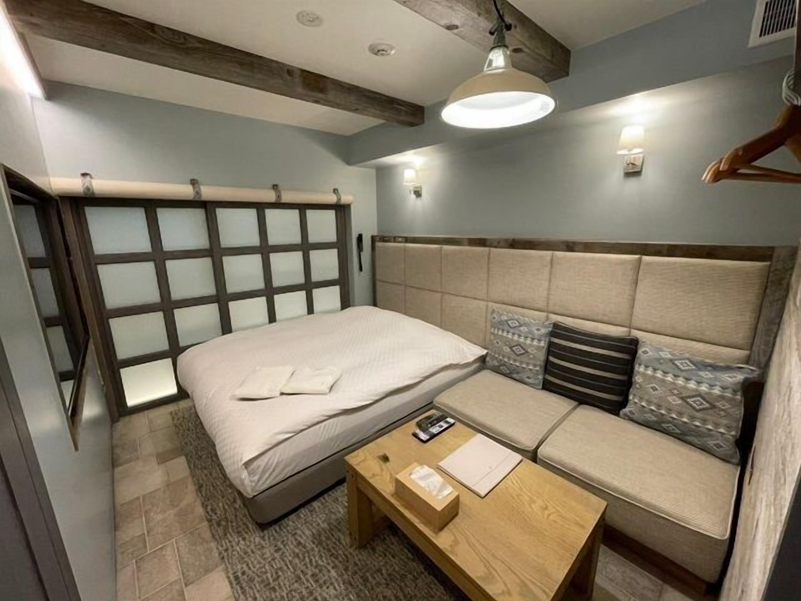 A bedroom with a bed, a sofa, a wooden coffee table, and a hanging light fixture.
