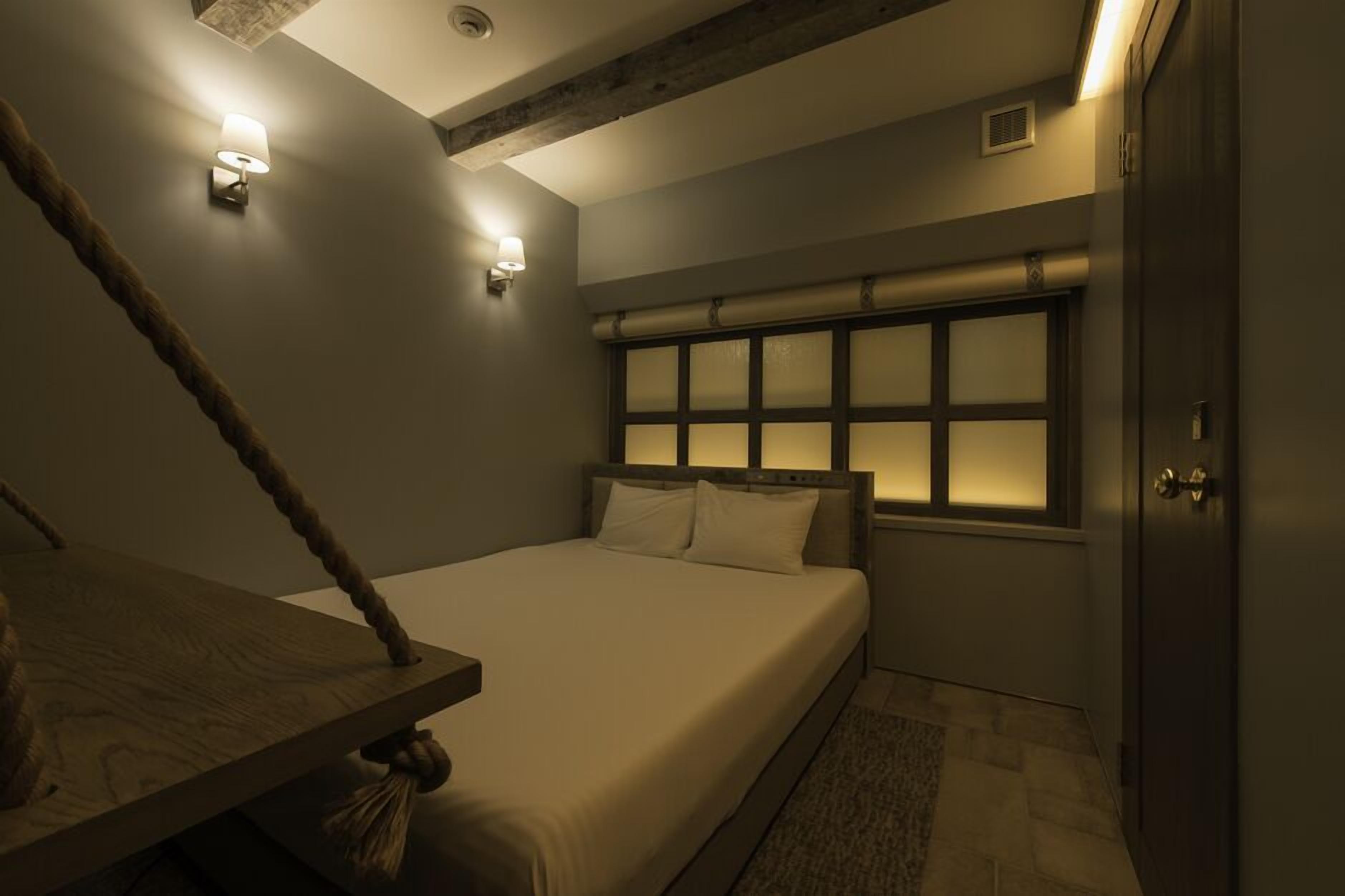 A bedroom with a bed, a wooden headboard, a window with frosted glass, and a wall-mounted light fixture.