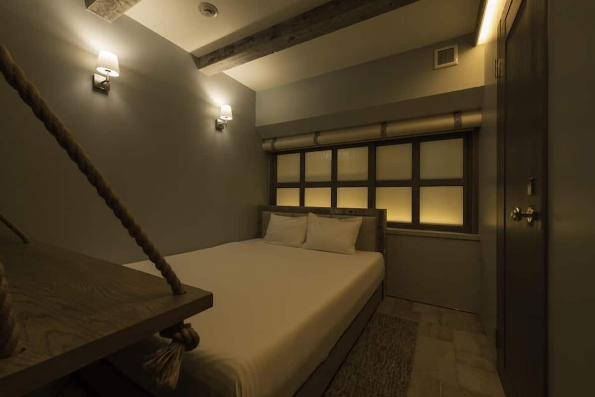 Une chambre à coucher avec un lit, une tête de lit en bois, une fenêtre à verre dépoli et un luminaire fixé au mur.
