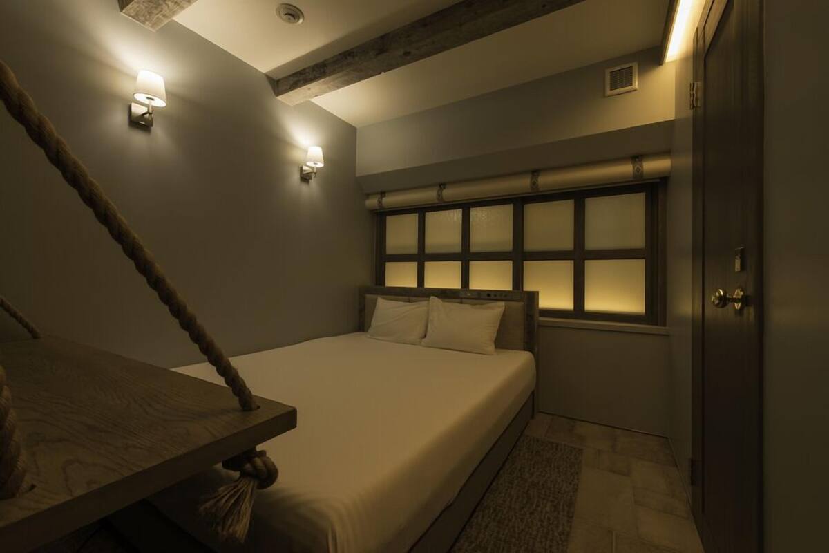 A bedroom with a bed, a wooden headboard, a window with frosted glass, and a wall-mounted light fixture.