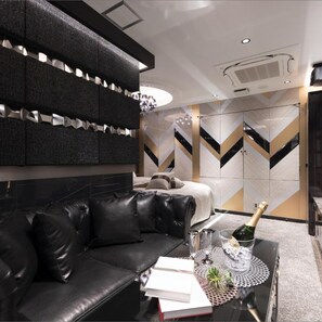 A modern living room with a black leather sofa, a glass coffee table with a book and a bottle, and a decorative wall with geometric patterns. - Hotel Kabuki (Tokyo)