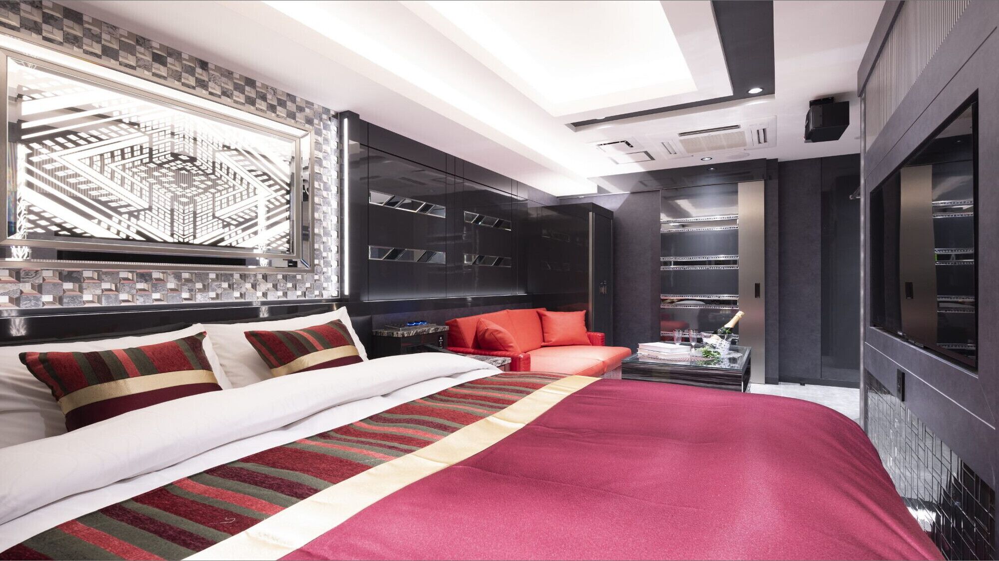 A modern bedroom with a large bed, a red sofa, and a view of a cityscape through a window.