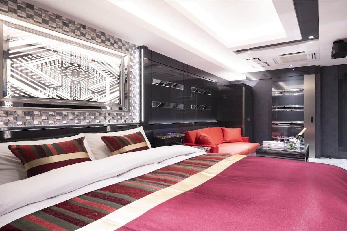 Une chambre moderne avec un grand lit, un canapé rouge et une vue sur le paysage urbain par la fenêtre.