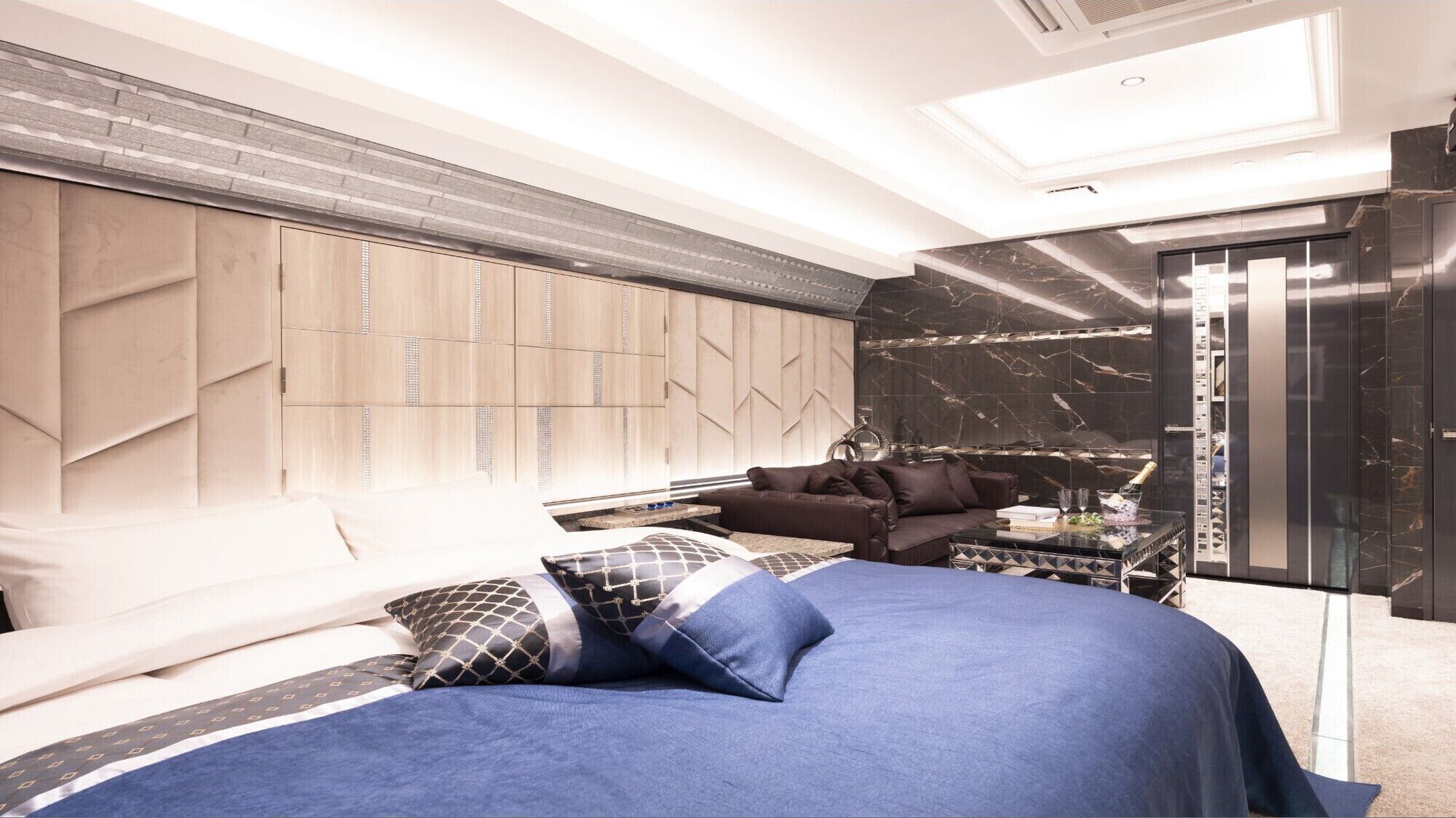 A modern bedroom with a bed, a sofa, a glass coffee table, and a minibar.