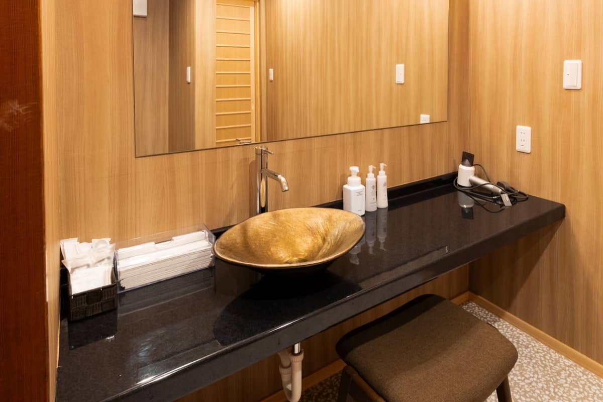 Ein Badezimmer mit einem großen Spiegel, einer schwarzen Ablagefläche, einem beigefarbenen Waschbecken, einem Handtuchhalter und einer Sitzbank.