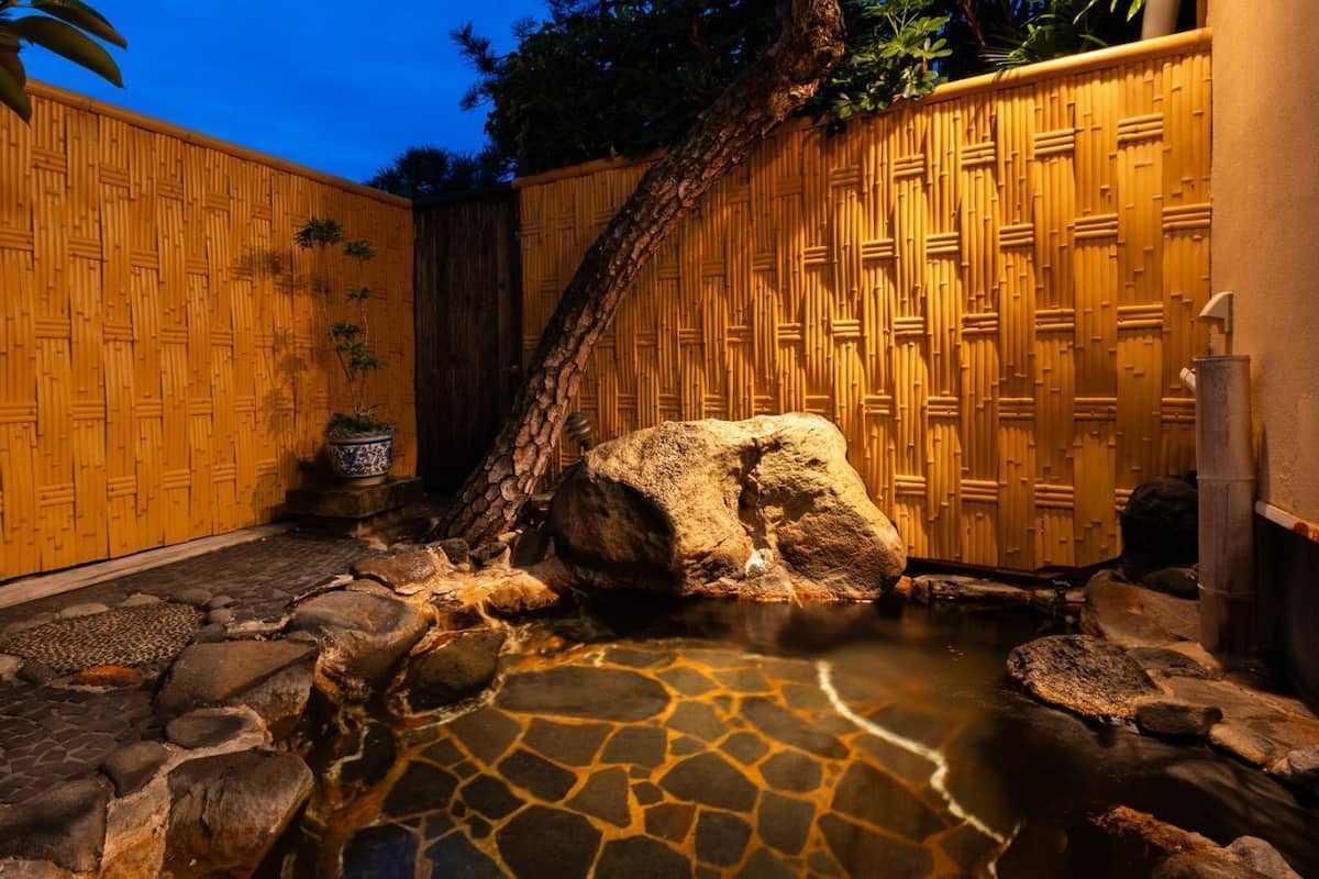 Ein Bambuszaun, eine Felsformation und ein kleines Wasserelement in einer Gartenanlage.