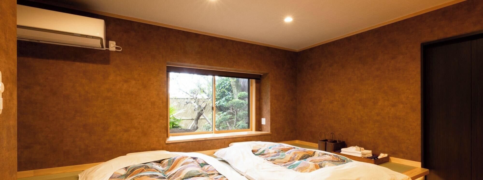 Ein Schlafzimmer mit zwei Betten, einem Fenster mit Blick auf Grünflächen, einer Wand-Klimaanlage und einer dunklen Tür.