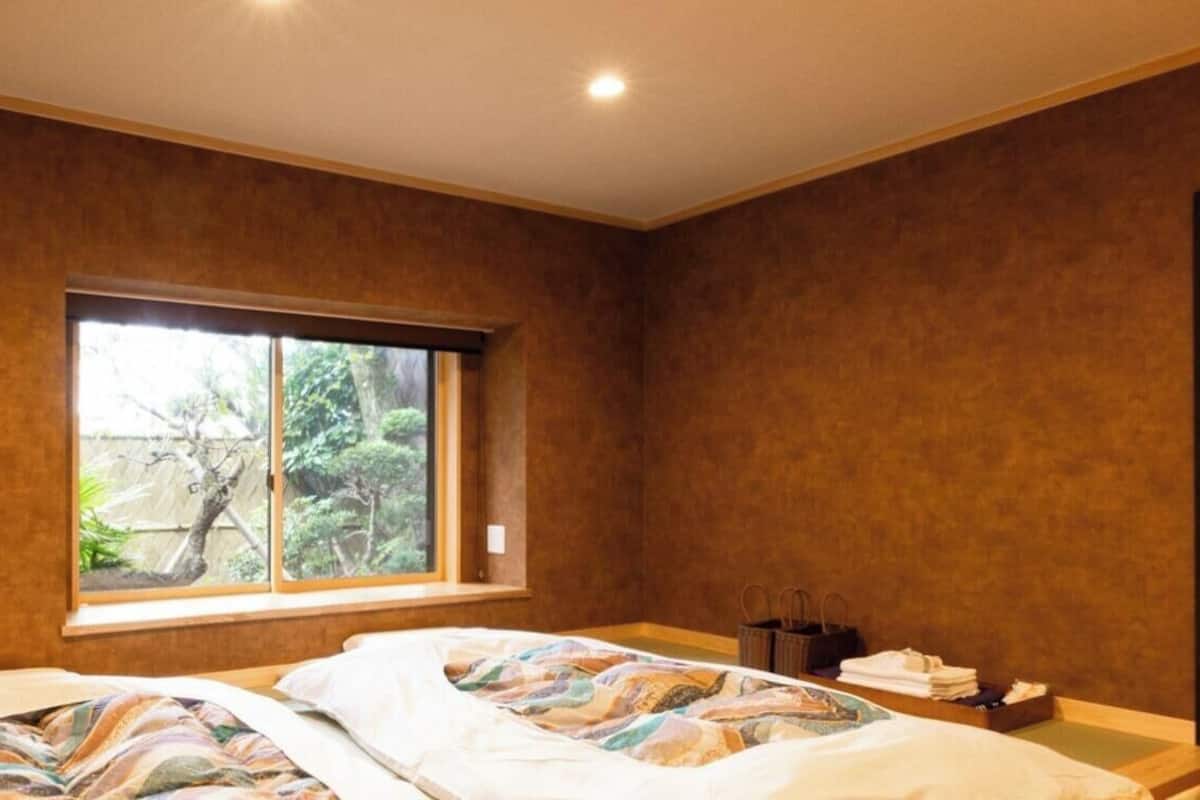 Ein Schlafzimmer mit zwei Betten, einem Fenster mit Blick auf Grünflächen, einer Wand-Klimaanlage und einer dunklen Tür.