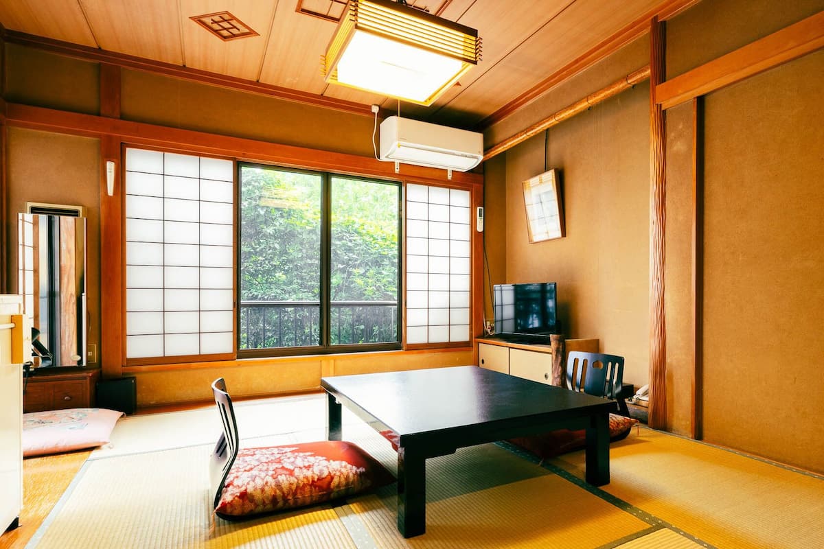 Ein traditioneller japanischer Raum mit Tatami-Böden, einem niedrigen Tisch, einem Fernseher und Schiebetüren.