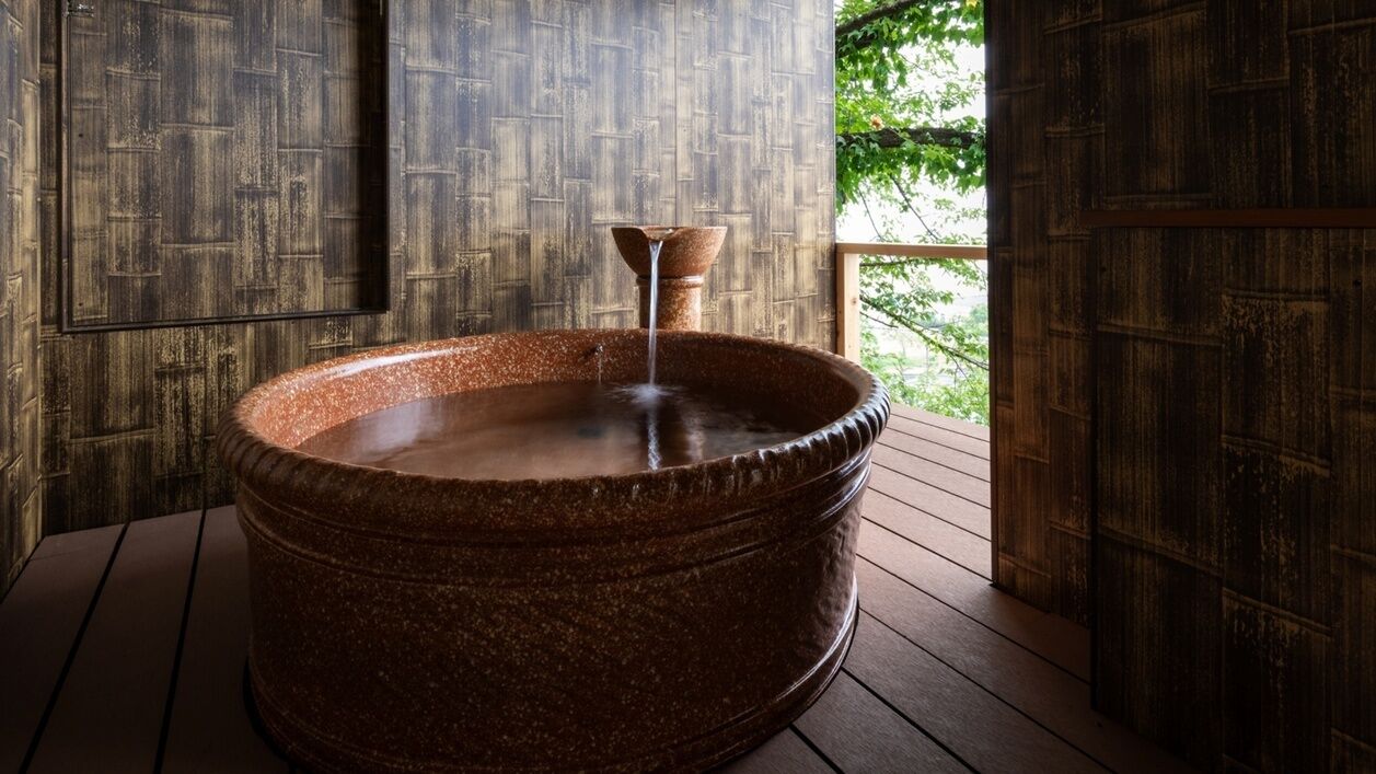 Ein Steintonne mit Wasserhahn auf einer Holzterrasse mit Blick ins Grüne.