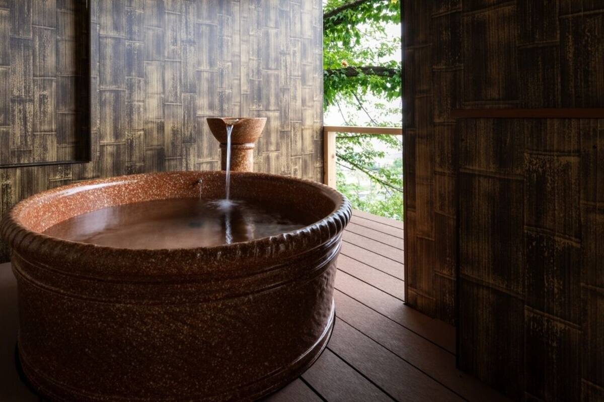 Ein Steintonne mit Wasserhahn auf einer Holzterrasse mit Blick ins Grüne.