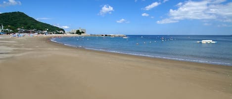 A wide sandy beach with a clear blue sky and a few boats in the water.