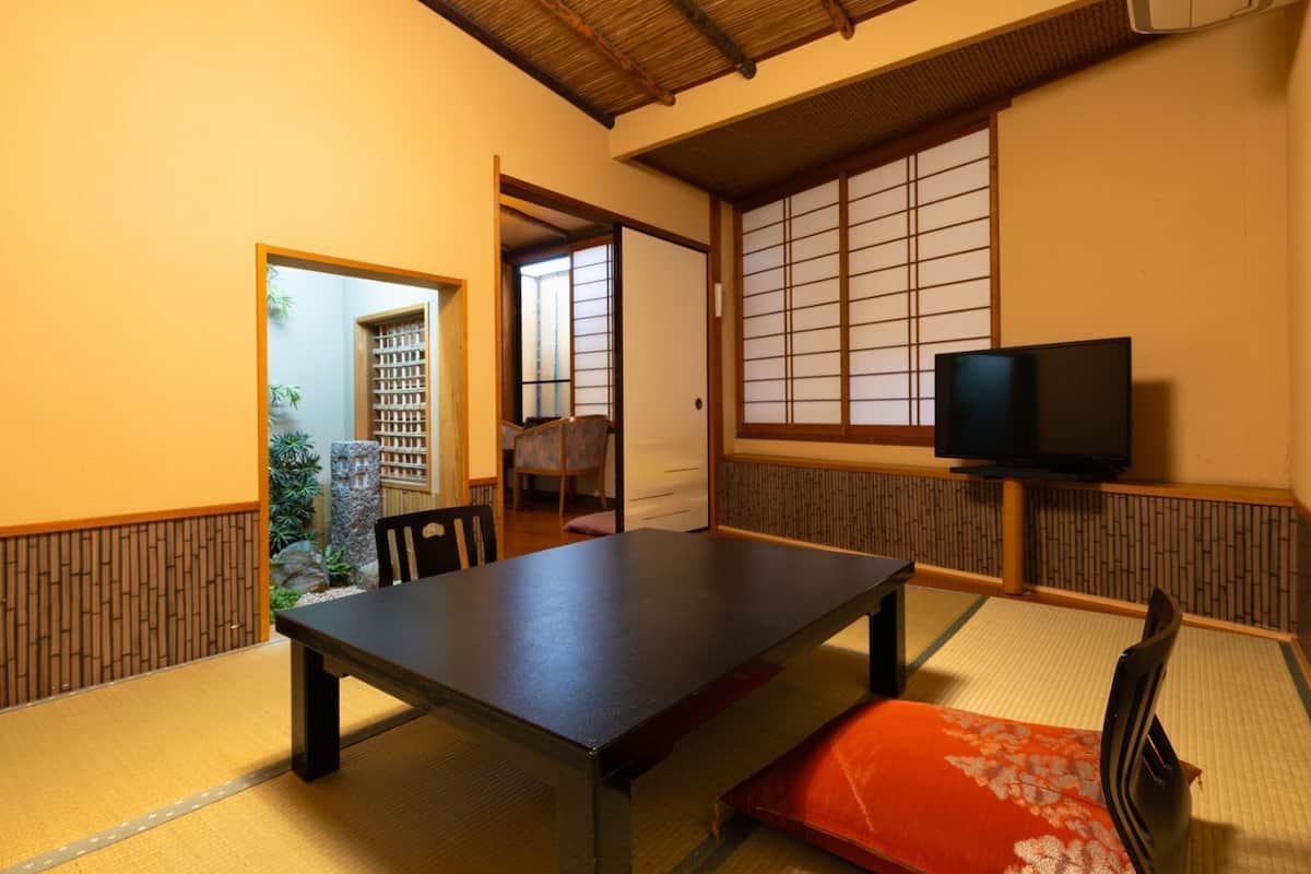 Ein traditioneller japanischer Raum mit Tatami-Böden, einem niedrigen Tisch, einem Fernseher und Schiebetüren.
