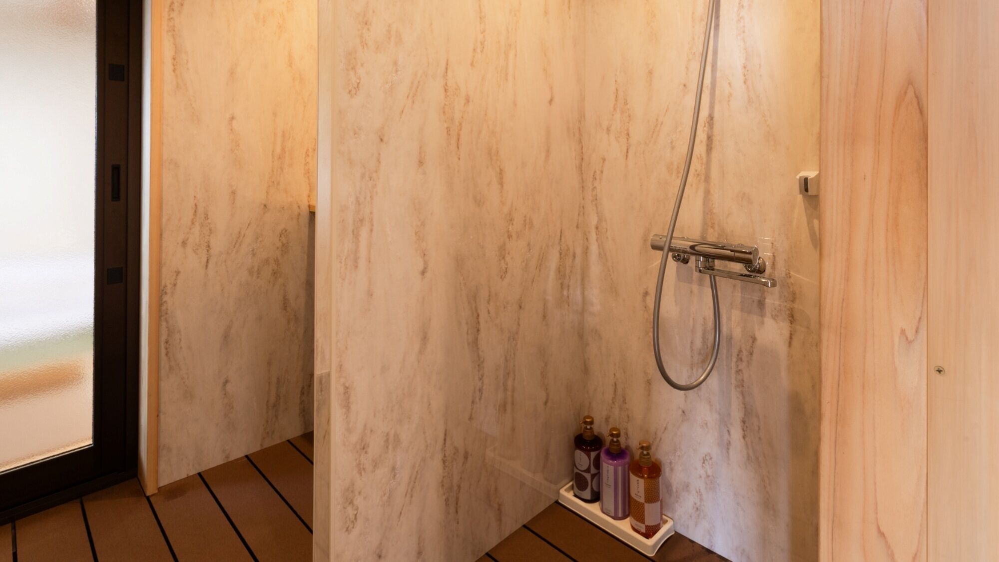 Ein Badezimmer mit Marmorwand, einer Dusche inklusive Handbrause und einem Ablagebereich für Toilettenartikel.