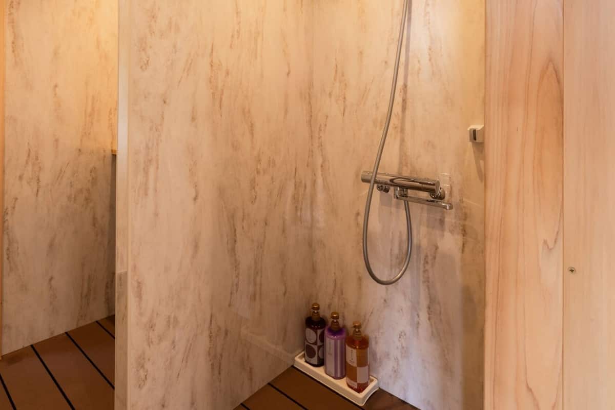 Ein Badezimmer mit Marmorwand, einer Dusche inklusive Handbrause und einem Ablagebereich für Toilettenartikel.