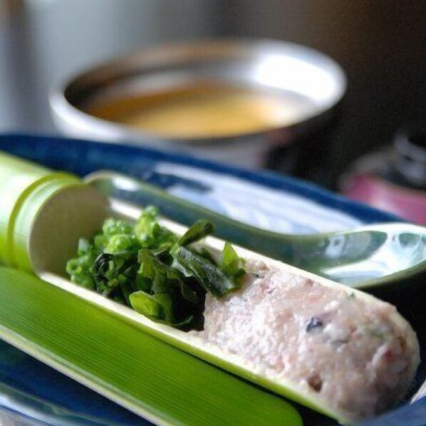 A dish with meat and greens on a plate with a bowl of soup in the background.