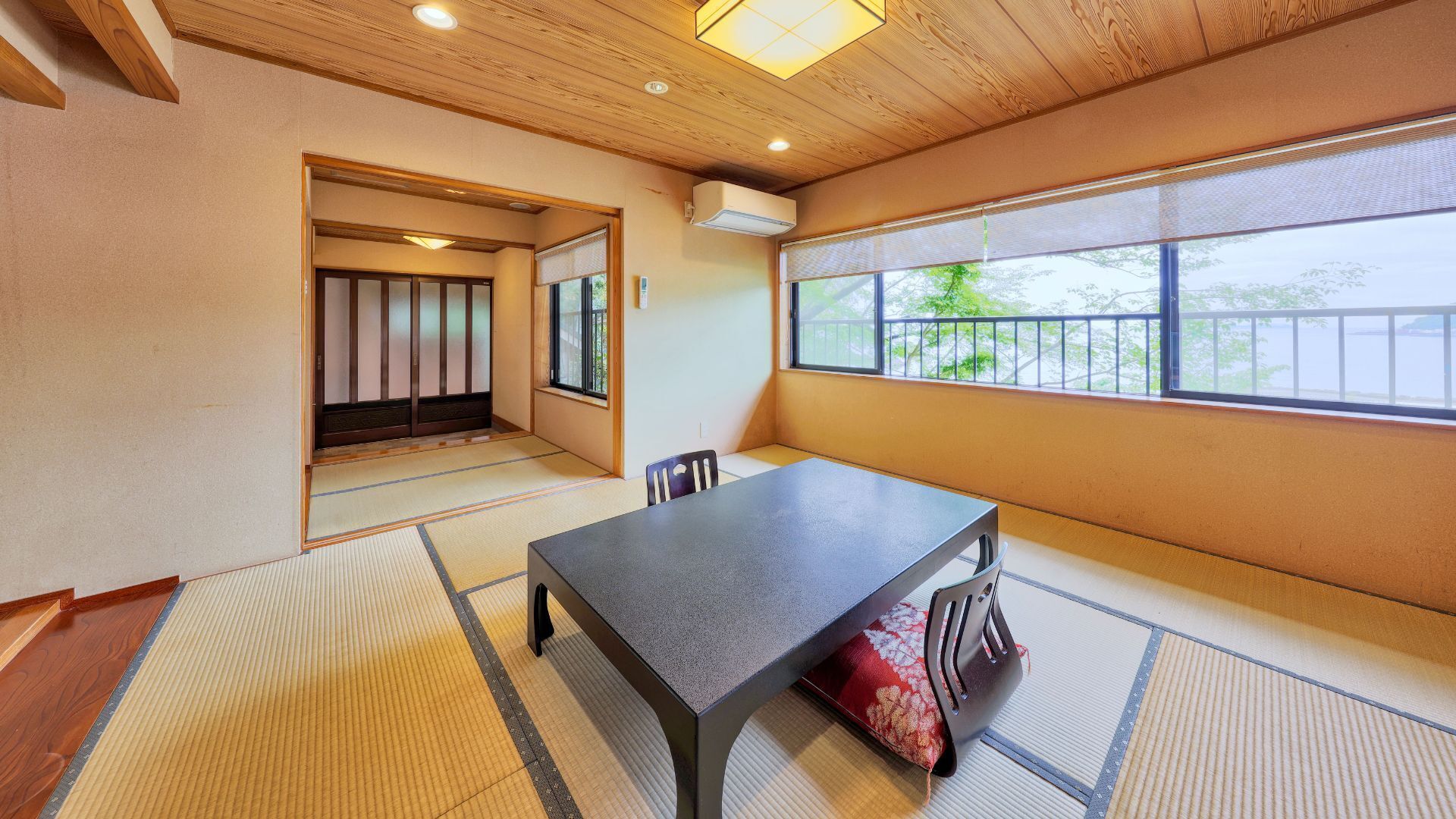 Ein Zimmer mit Tatami-Boden, einem niedrigen Tisch, einem Stuhl, einer Schiebetür und einem großen Fenster mit Aussicht.