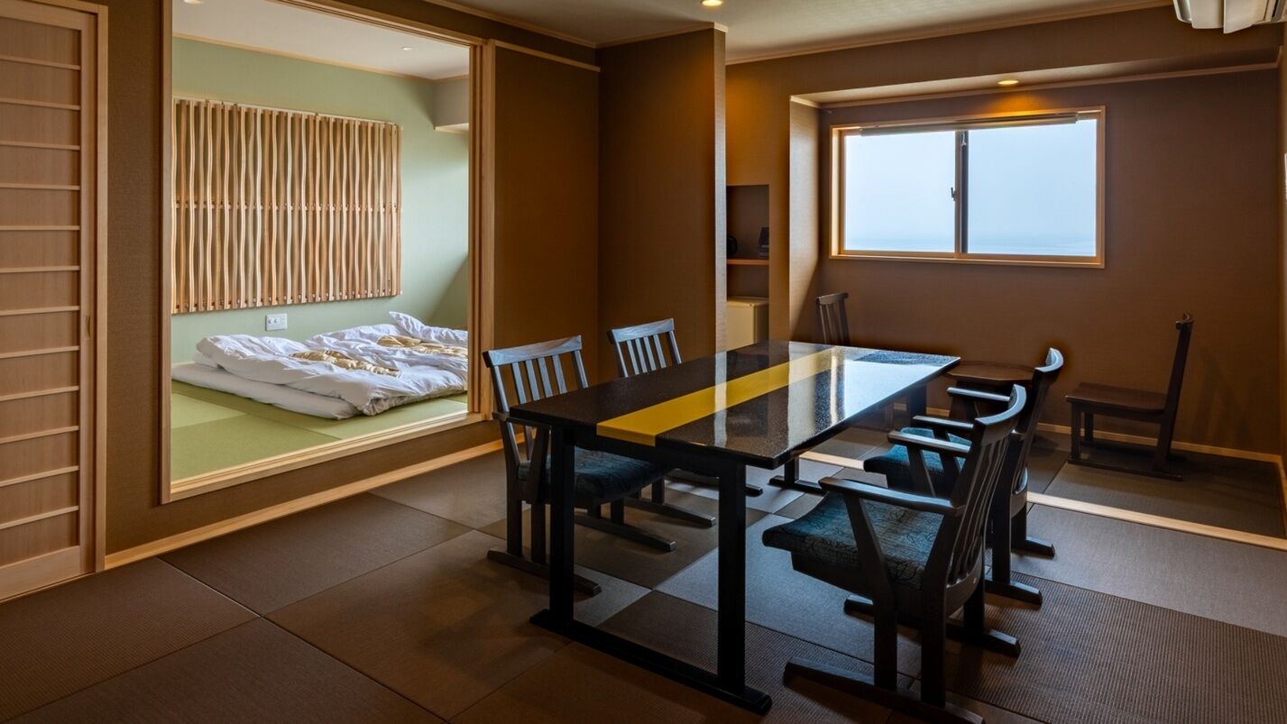 Ein Hotelzimmer mit Bett, einem Esstisch mit Stühlen, einem Fenster und Blick aufs Meer.