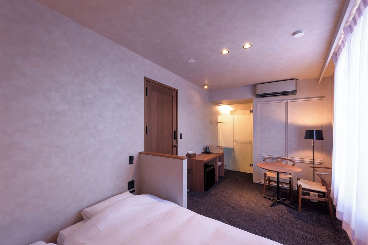 A hotel room with a bed, desk, chair, and a small kitchenette.