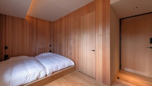 A bedroom with a bed, wooden walls, a door, and a ceiling light.