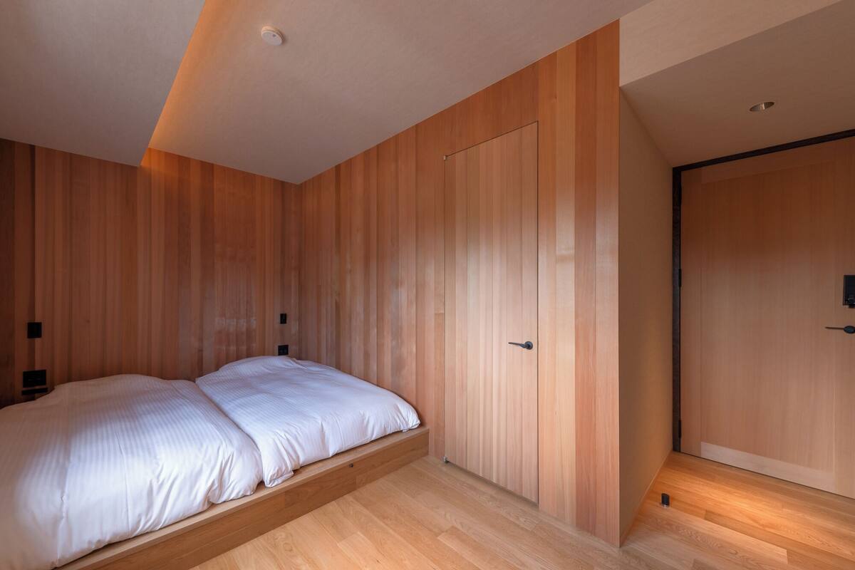 A bedroom with a bed, wooden walls, a door, and a ceiling light.