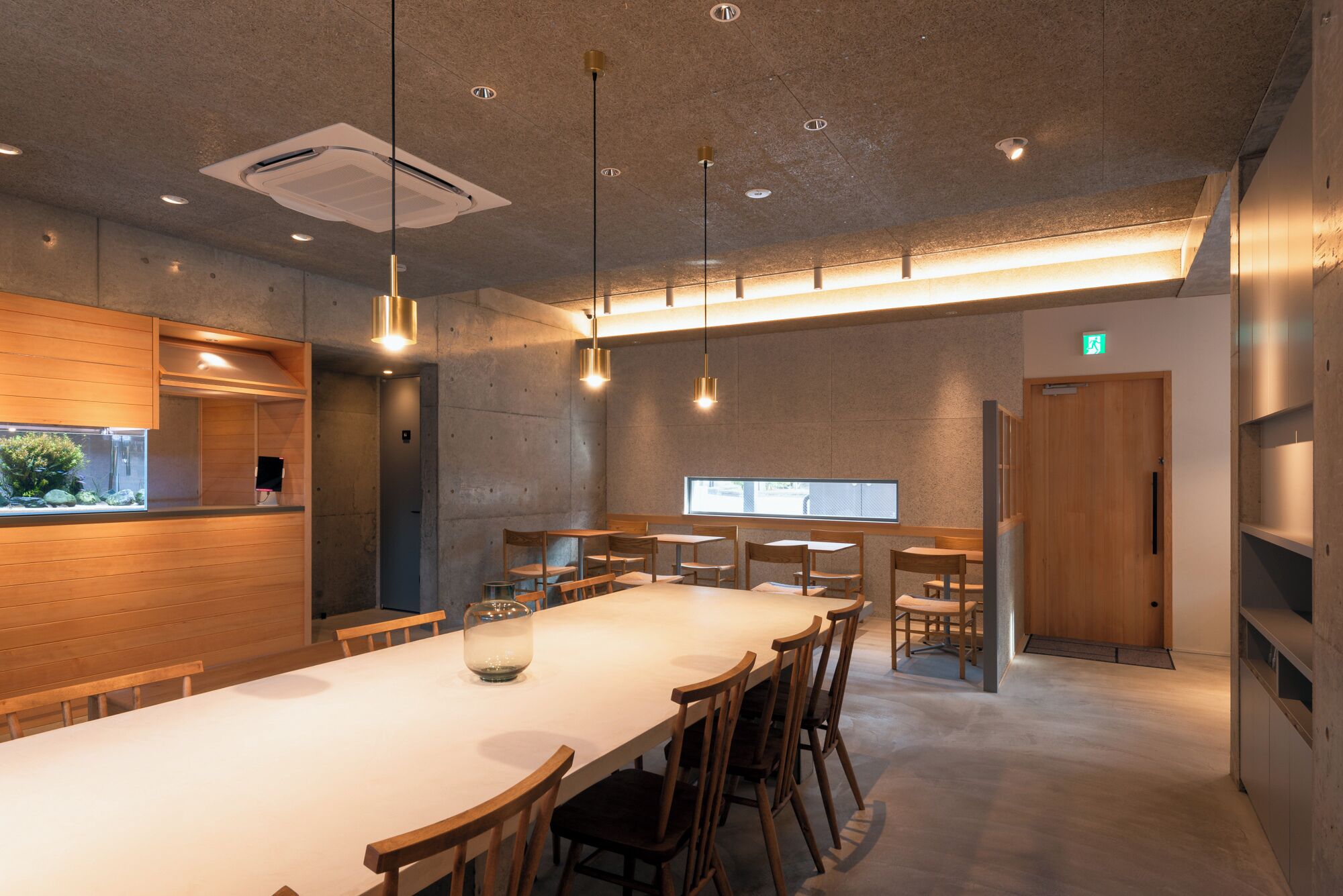 A modern dining area with a long table, chairs, pendant lights, and a view of the outdoors.