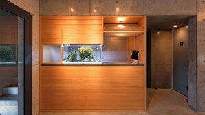 A reception desk with a wooden finish, a glass aquarium with plants, and a black monitor.