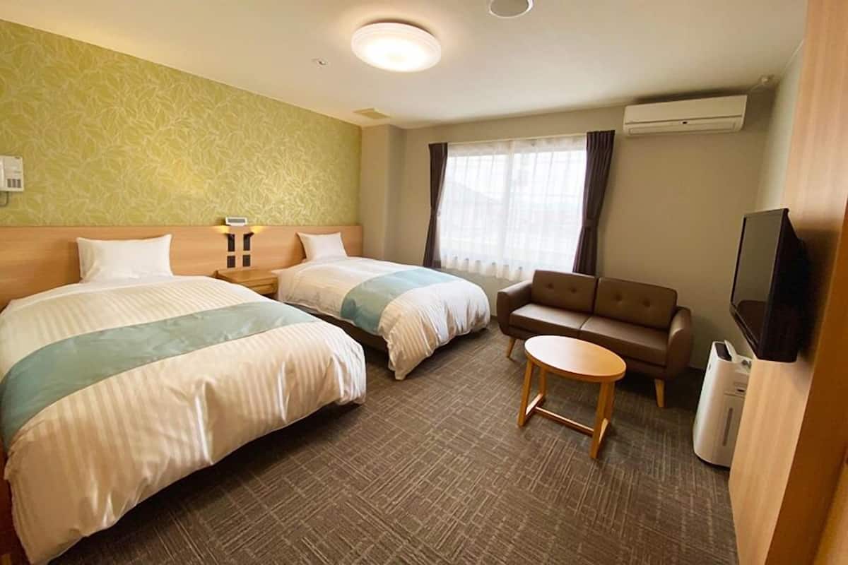 Habitación de hotel con dos camas, un sofá, una mesita, un televisor y un equipo de aire acondicionado.