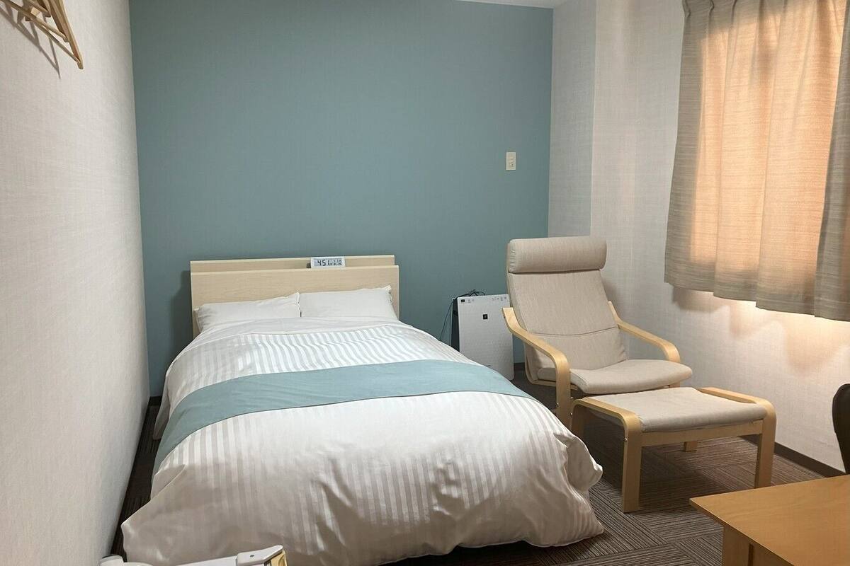 Habitación de hotel con cama, una silla, una mesa y ventana con cortinas.