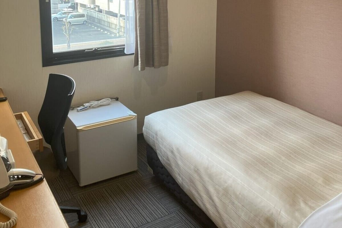 Habitación de hotel con cama, escritorio, silla y ventana con vistas a edificios.