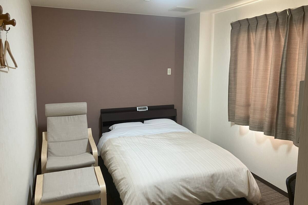 Una habitación de hotel con una cama, una silla, un reloj de pared y una ventana con cortinas.