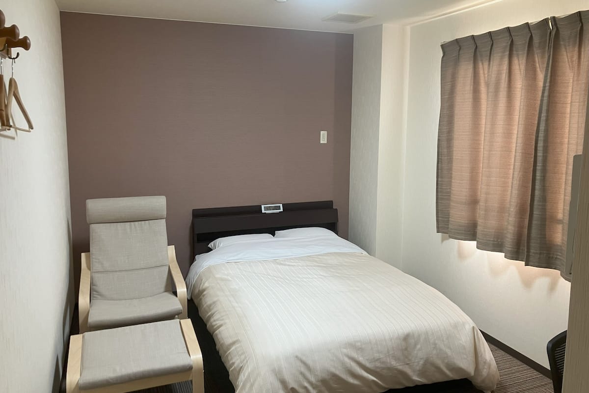 Una habitación de hotel con una cama, una silla, un reloj de pared y una ventana con cortinas.