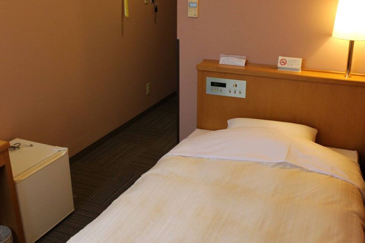 Una habitación de hotel con una cama, un escritorio, un cubo de basura y un panel de control en la pared.