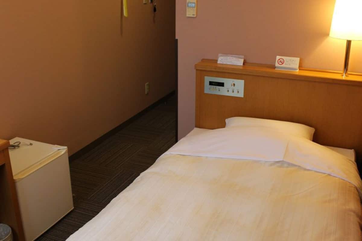 Una habitación de hotel con una cama, un escritorio, un cubo de basura y un panel de control en la pared.