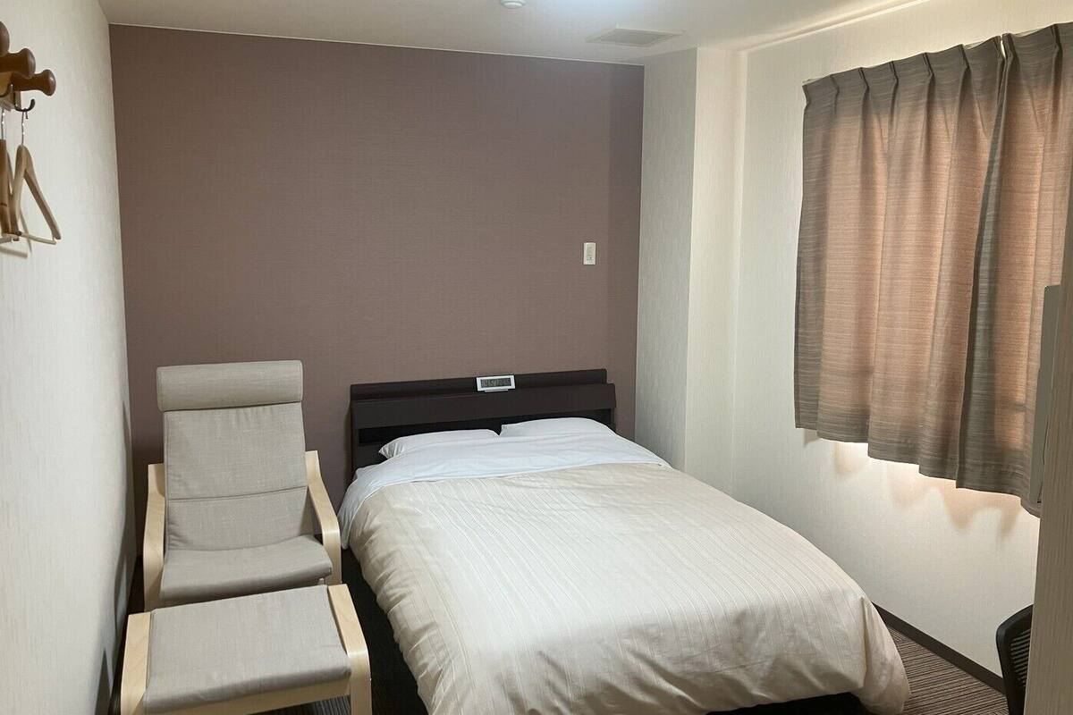 Una cama individual con cabecera, una silla, un reloj de pared y una ventana con cortinas.
