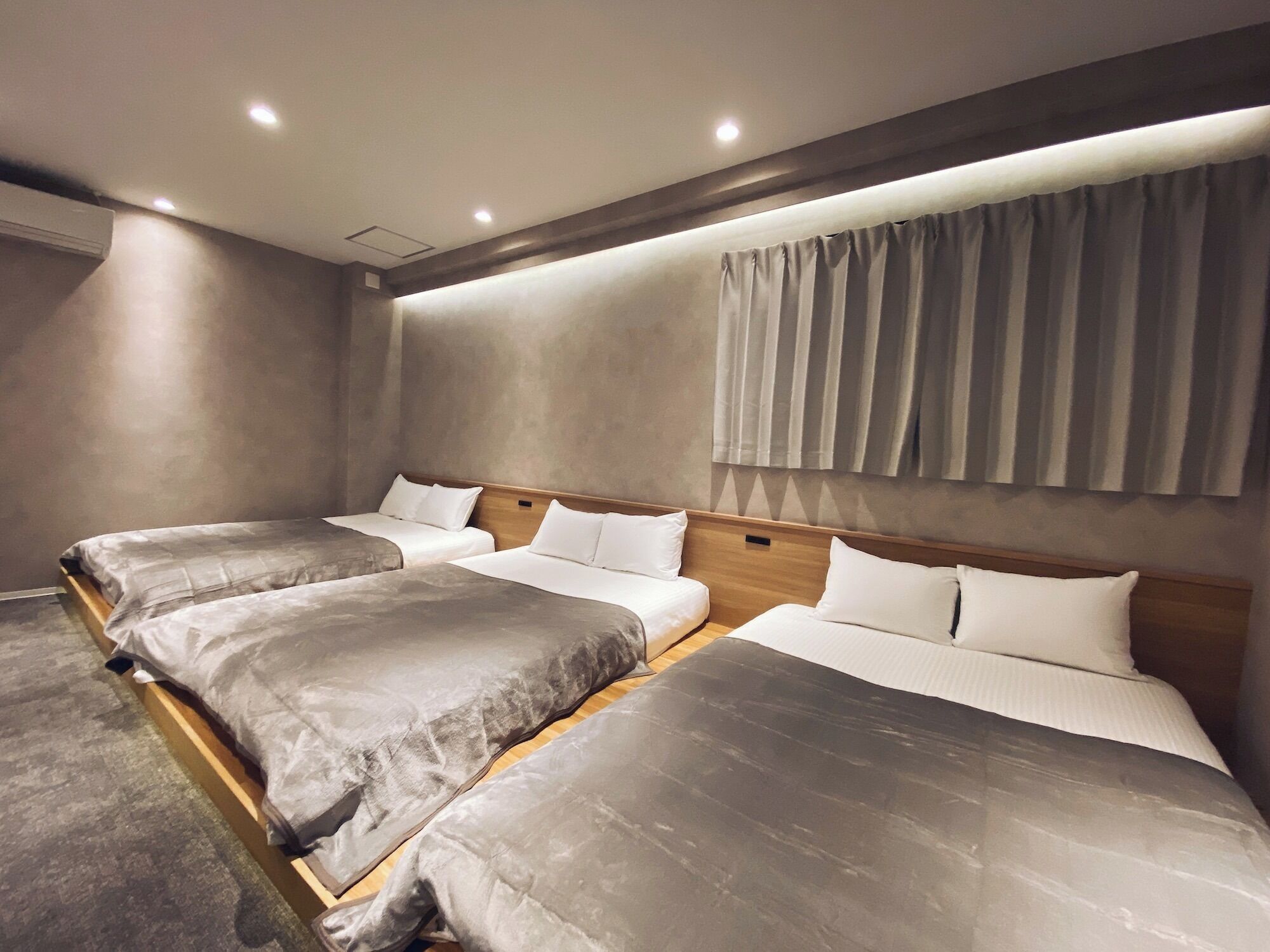 A hotel room with three beds arranged in a row, a large window with curtains, and a modern design.