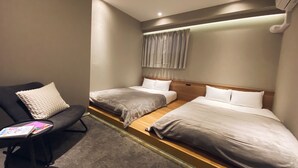 Habitación de hotel con dos camas, un pequeño espacio para sentarse y una ventana con cortinas.