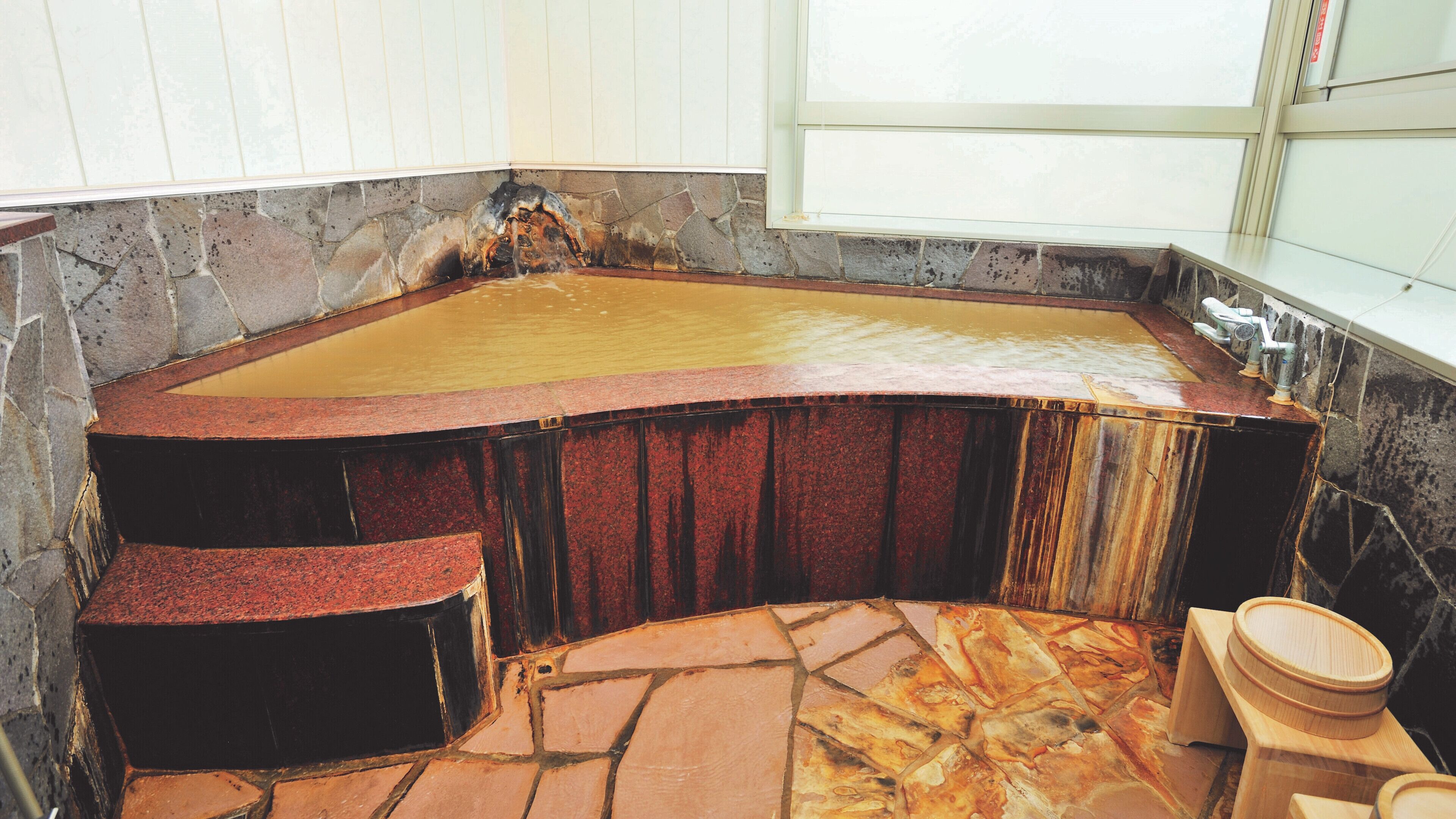 A stone bathtub with a wooden seat and a wooden basin.