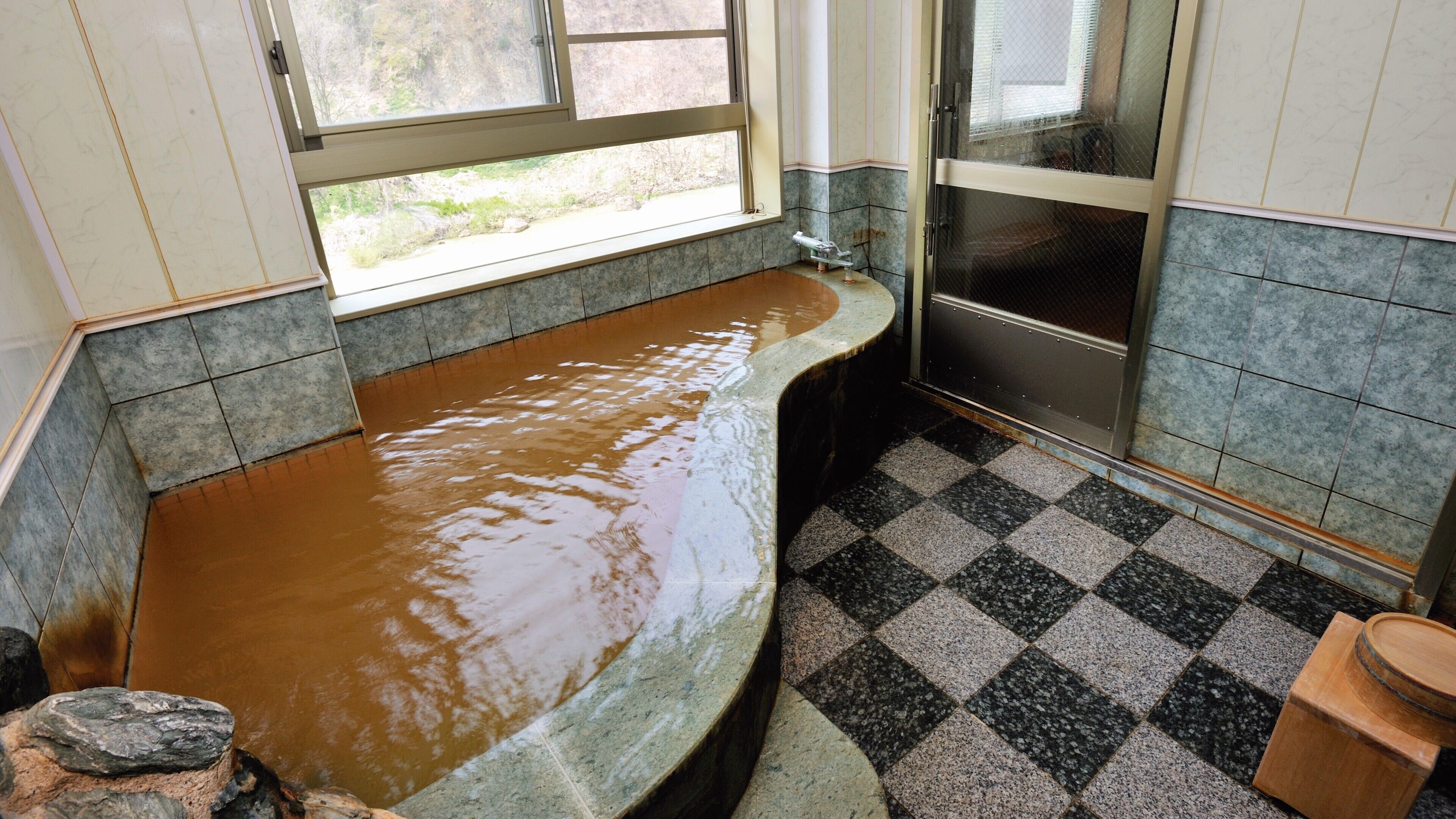 A bathroom with a large bathtub filled with water, a window, and a checkered floor.