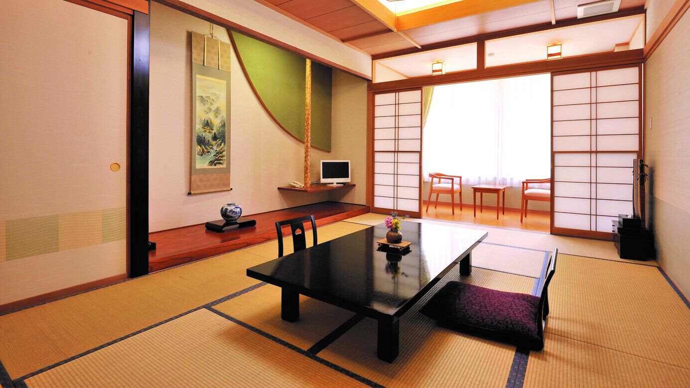 Una habitación japonesa tradicional con suelo de tatami, una mesa baja, sillas, un televisor y puertas correderas.