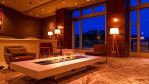 Un vestíbulo moderno con una chimenea central, asientos, ventanas amplias y vistas al exterior.