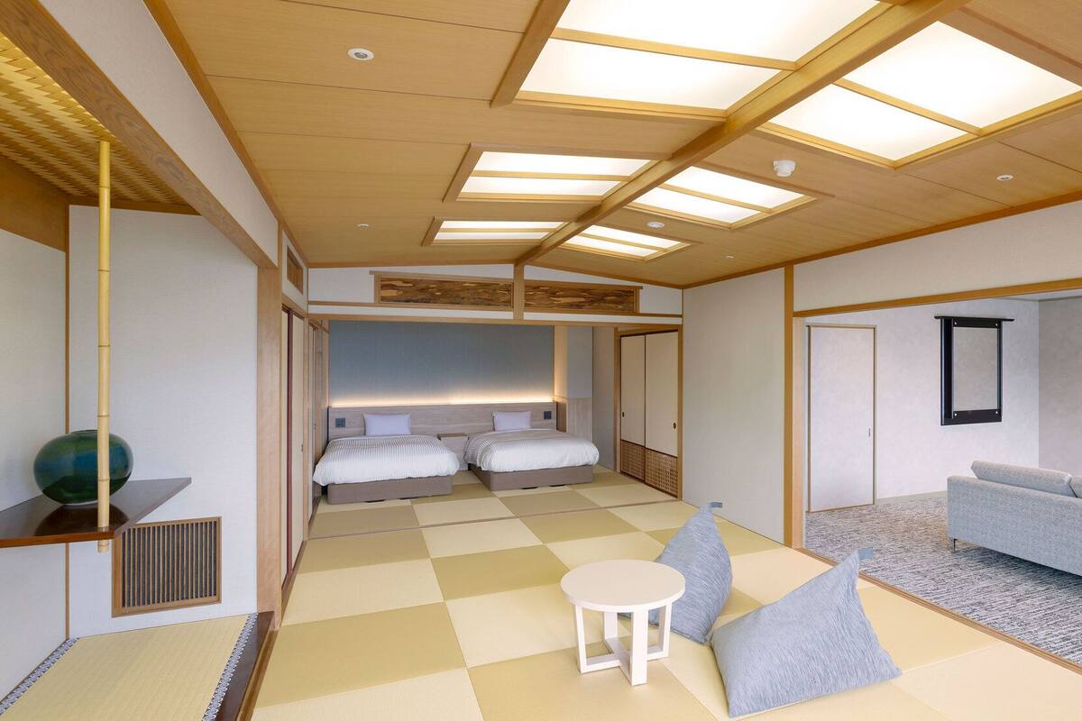 A modern hotel room with a checkered floor, a sofa, a TV, and a bed with two pillows.