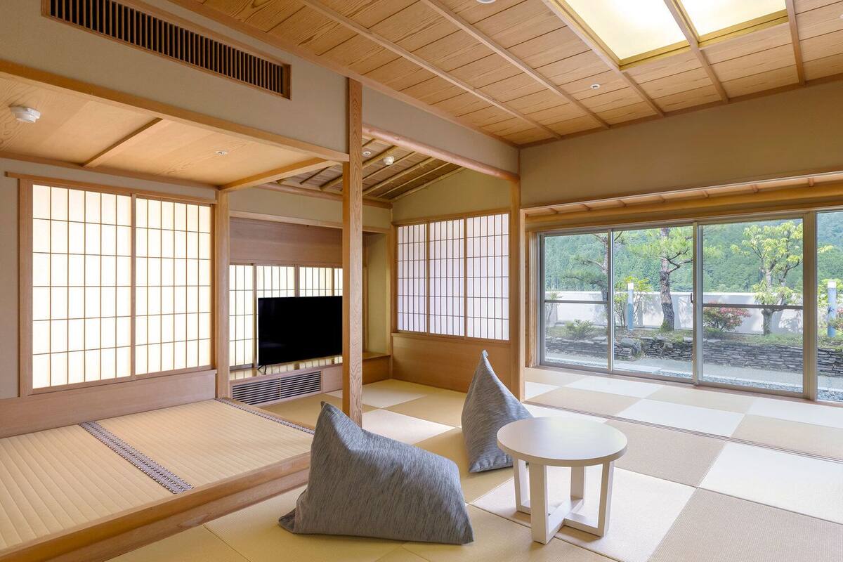 A traditional Japanese-style room with tatami flooring, a television, and a view of greenery outside.