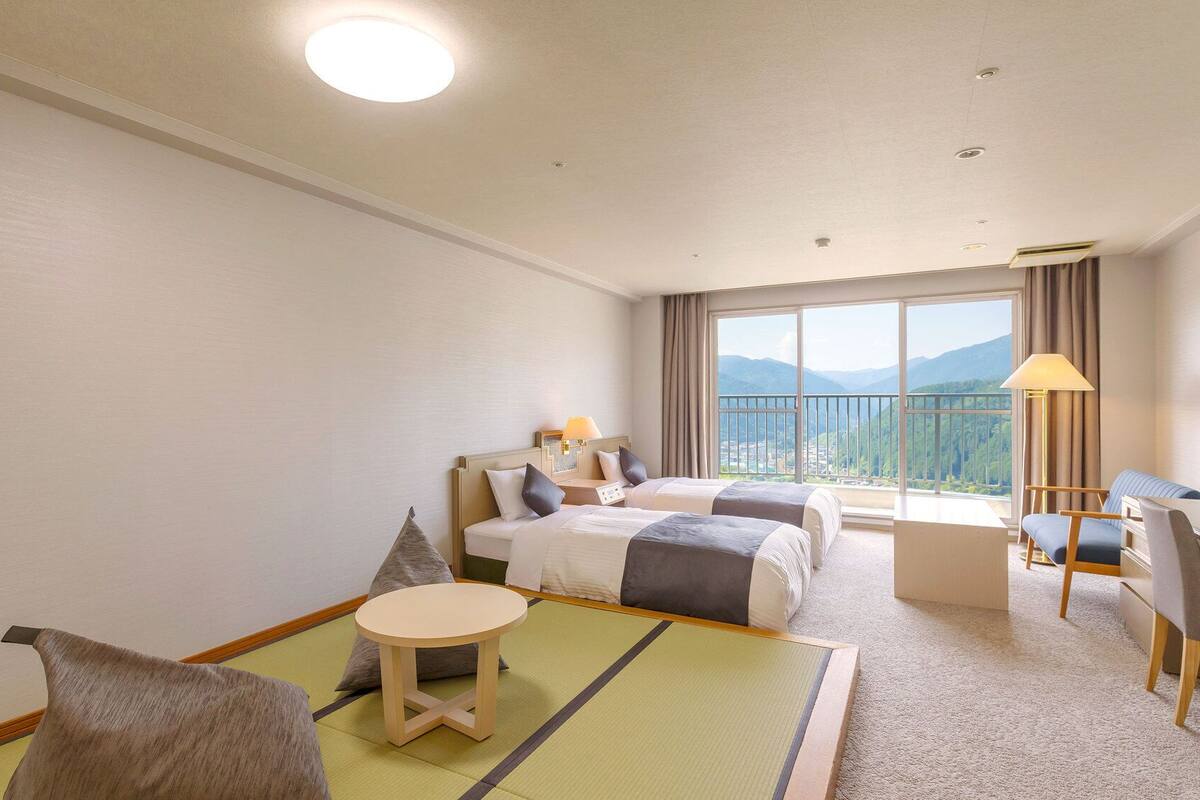 A hotel room with two beds, a desk, a chair, a table, and a view of mountains.