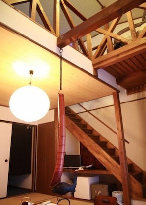 Una habitación con una escalera de madera, una lámpara colgante y un escritorio con un ordenador.