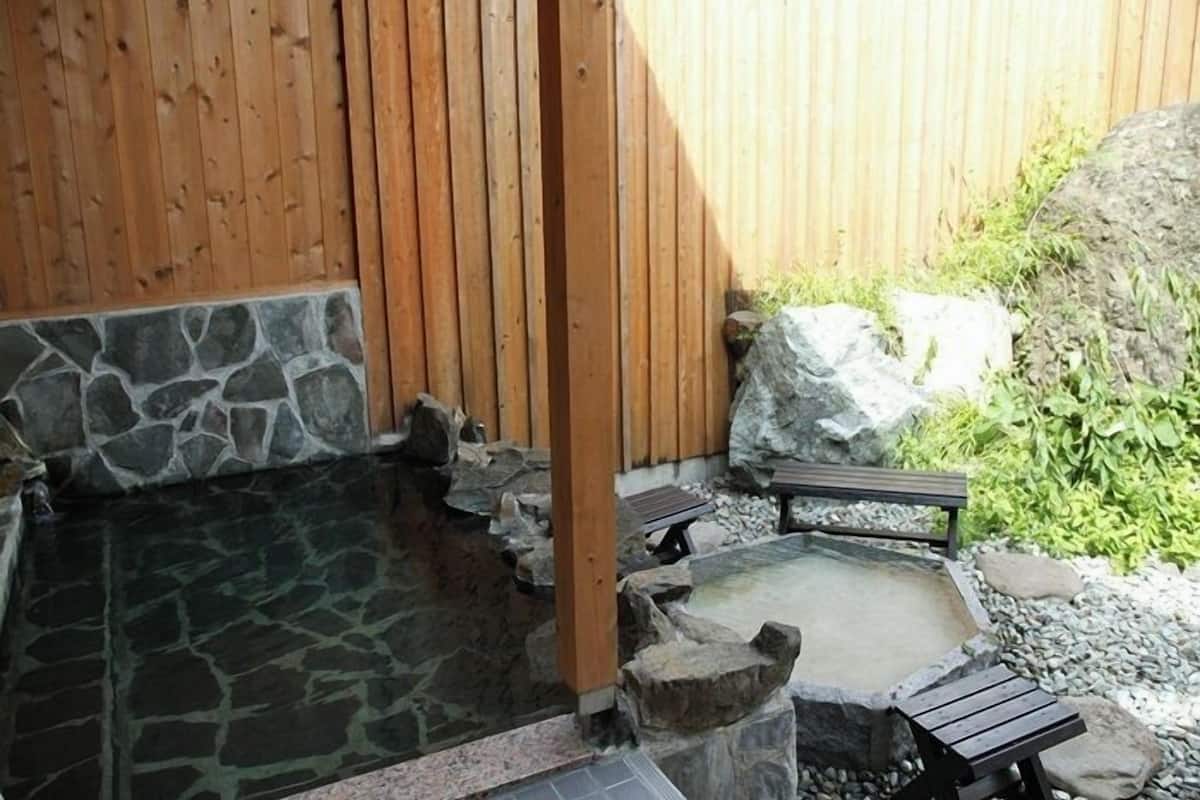 Un jacuzzi de piedra con bancos de madera, rodeado por una valla de madera y un muro de piedra.